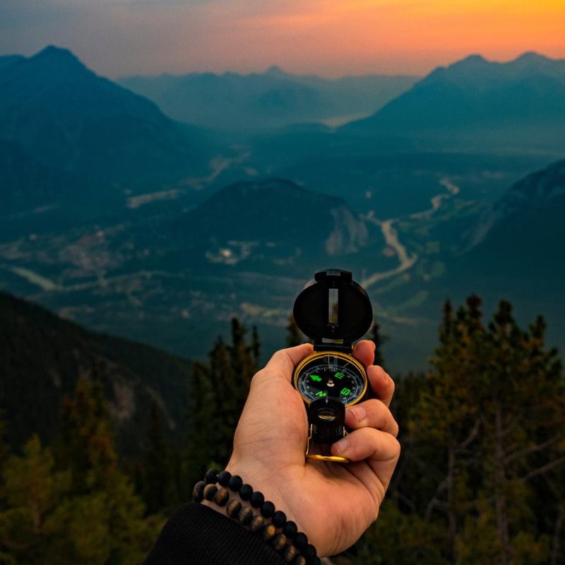hand holding compass with sunset over mountains in the background
