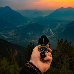 hand holding compass with sunset over mountains